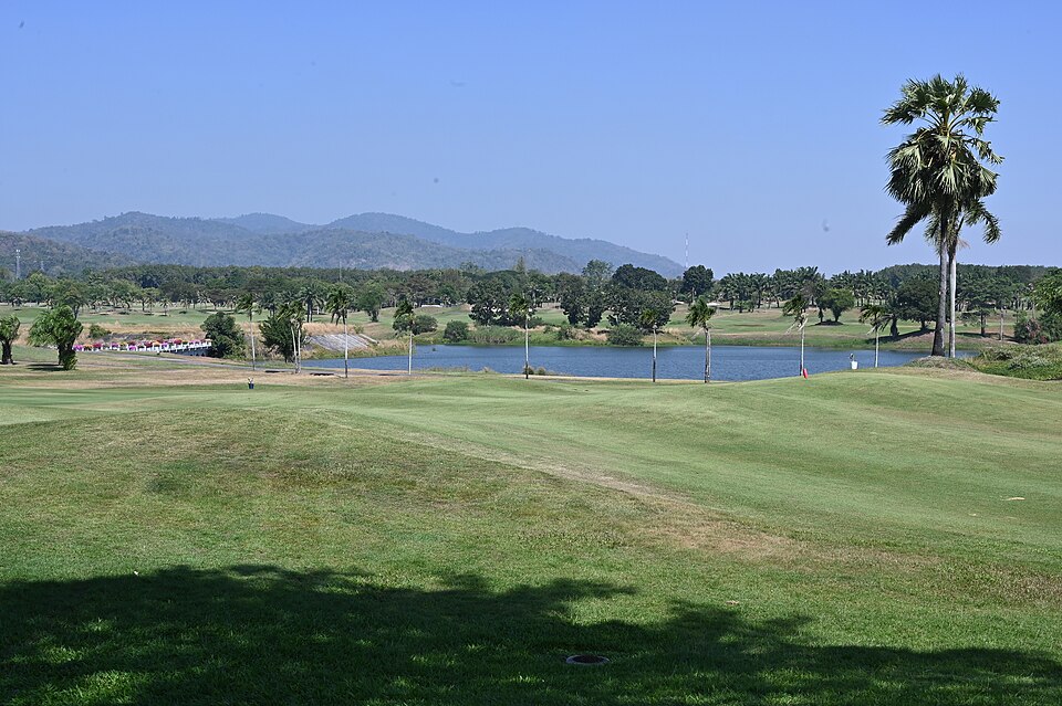 DSC 6936 Sunlit golf course fairway with a tranquil water hazard palm trees and rolling hills in the distance